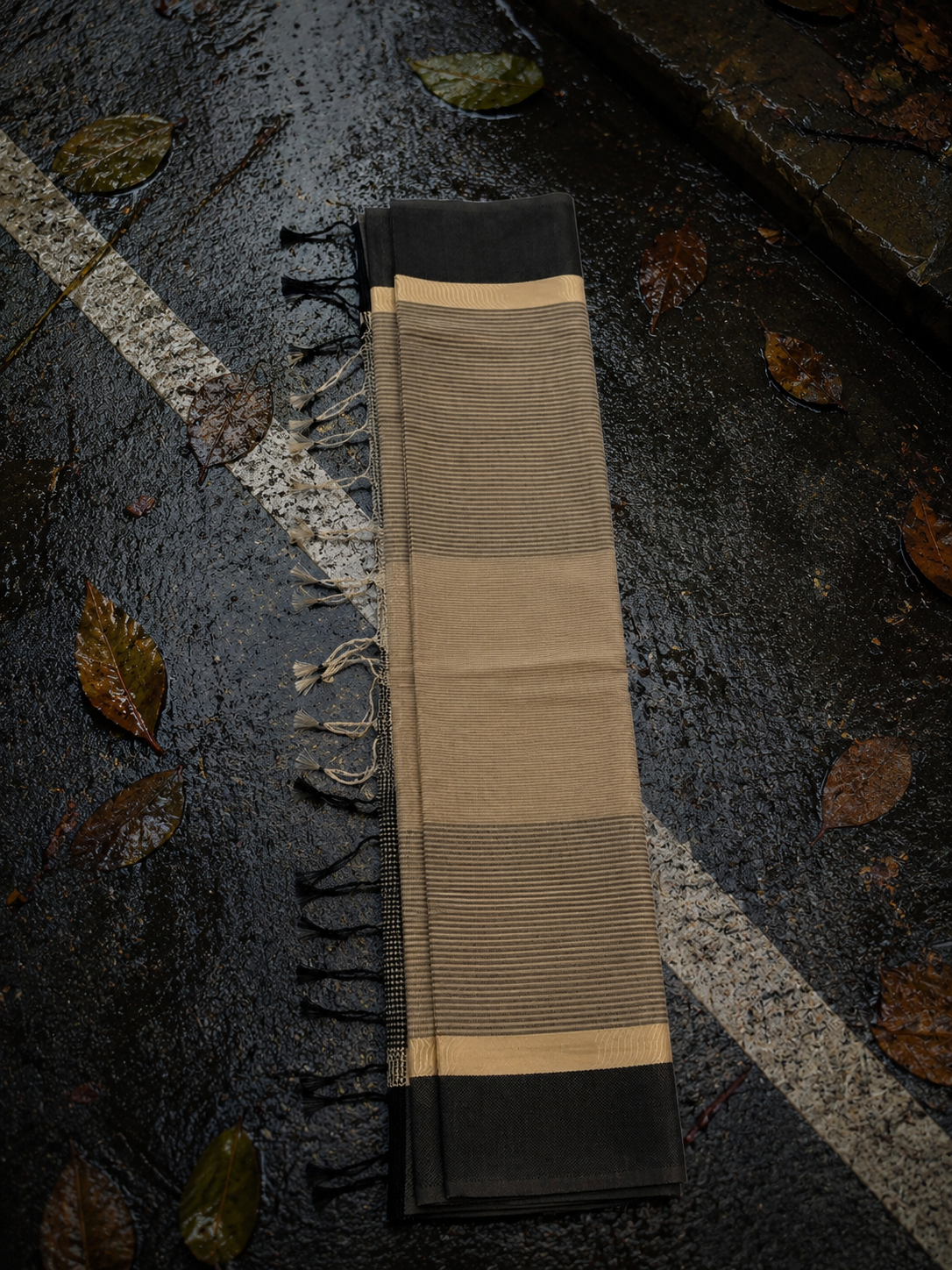 Folded beige handcrafted Chanderi saree featuring fine woven stripes, black border and handcrafted tassels.
